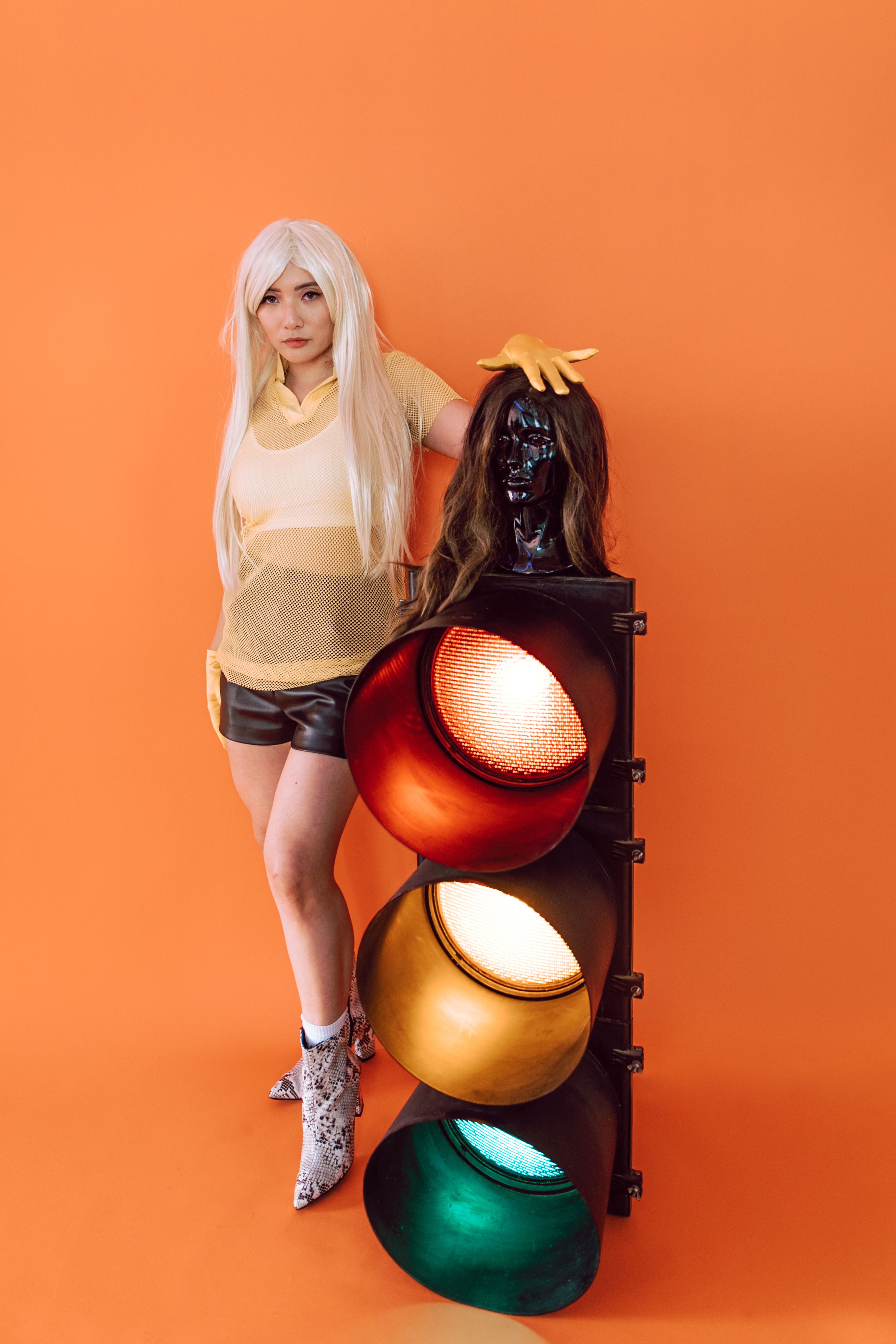 Fashion portrait of a woman in front of a vibrant backdrop with wigs and a traffic light.