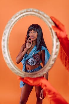 Stylish portrait of a woman through a decorative mirror on a bright orange background.