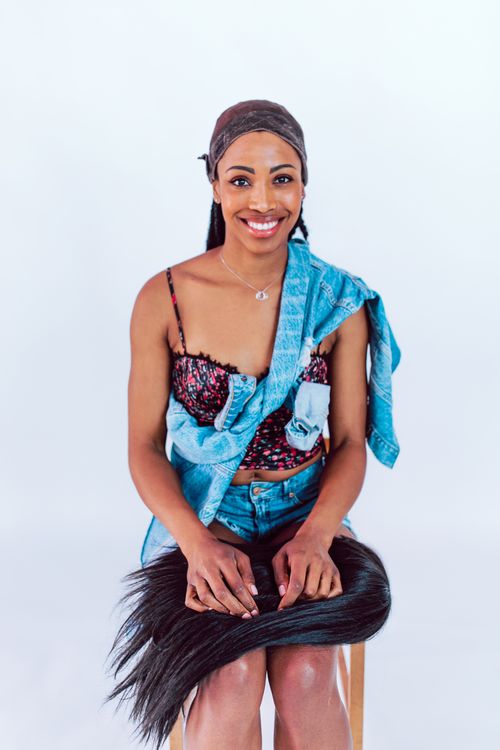 Free African American woman in denim sitting with hair extensions, smiling against a white background. Stock Photo