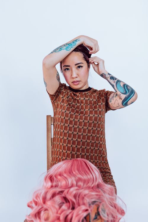 Free A tattooed woman adjusts her hair, wearing a patterned dress in a bright studio. Stock Photo