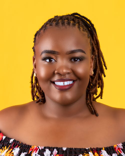 Positive pus size African American female with makeup smiling widely and looking at camera against yellow background