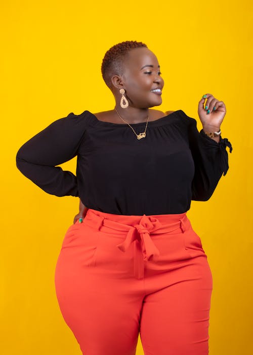 Free Young positive African American plus size female with hand on waist standing against bright yellow background and looking away Stock Photo