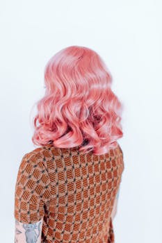Back view of a person with wavy pink hair and tattooed arm wearing a stylish patterned top.