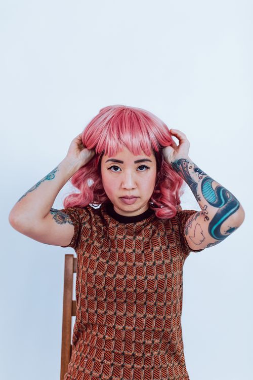 Free Vibrant portrait of a woman with a pink wig and tattooed arms indoors. Stock Photo
