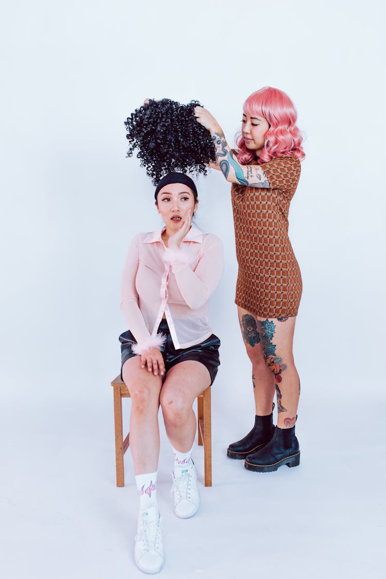 A Woman Putting A Wig On Another Woman