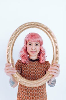 A woman with pink hair framed artfully in a vintage gold mirror, showcasing style.
