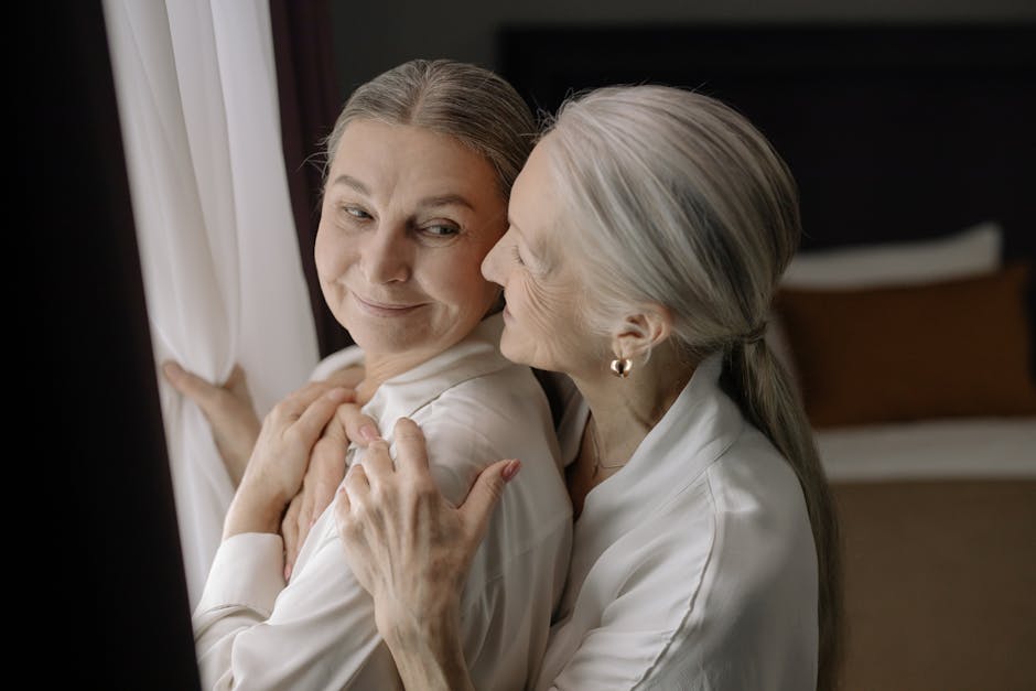 Two senior women sharing a tender moment in a warm embrace indoors.