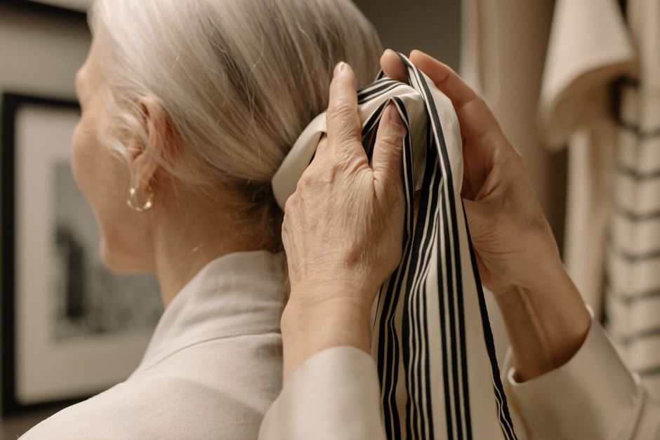 Elegant senior woman tying a striped scarf in her gray hair