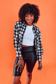 Portrait of a stylish woman wearing a plaid shirt and leather shorts against an orange backdrop.