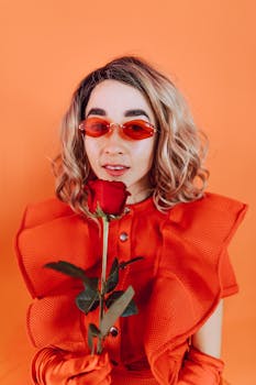 Fashion-forward woman in red attire holding a rose against an orange background.