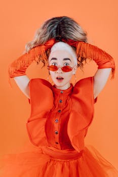 Eye-catching portrait of a woman in orange fashion holding a wig against an orange background.