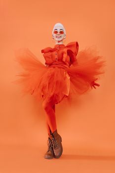 Colorful fashion portrait of a joyful woman in a striking orange dress with a playful pose and sunglasses.