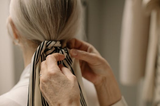 Close-up of hands tying a striped ribbon in gray hair, showcasing elegance.