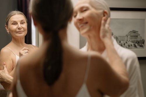 Free An elderly woman smiles warmly at her reflection in a mirror, showing contentment and self-love. Stock Photo
