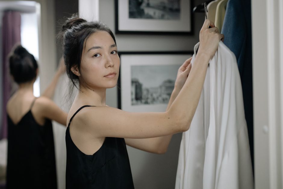 Woman in a black dress looking thoughtfully at clothes in wardrobe indoors.