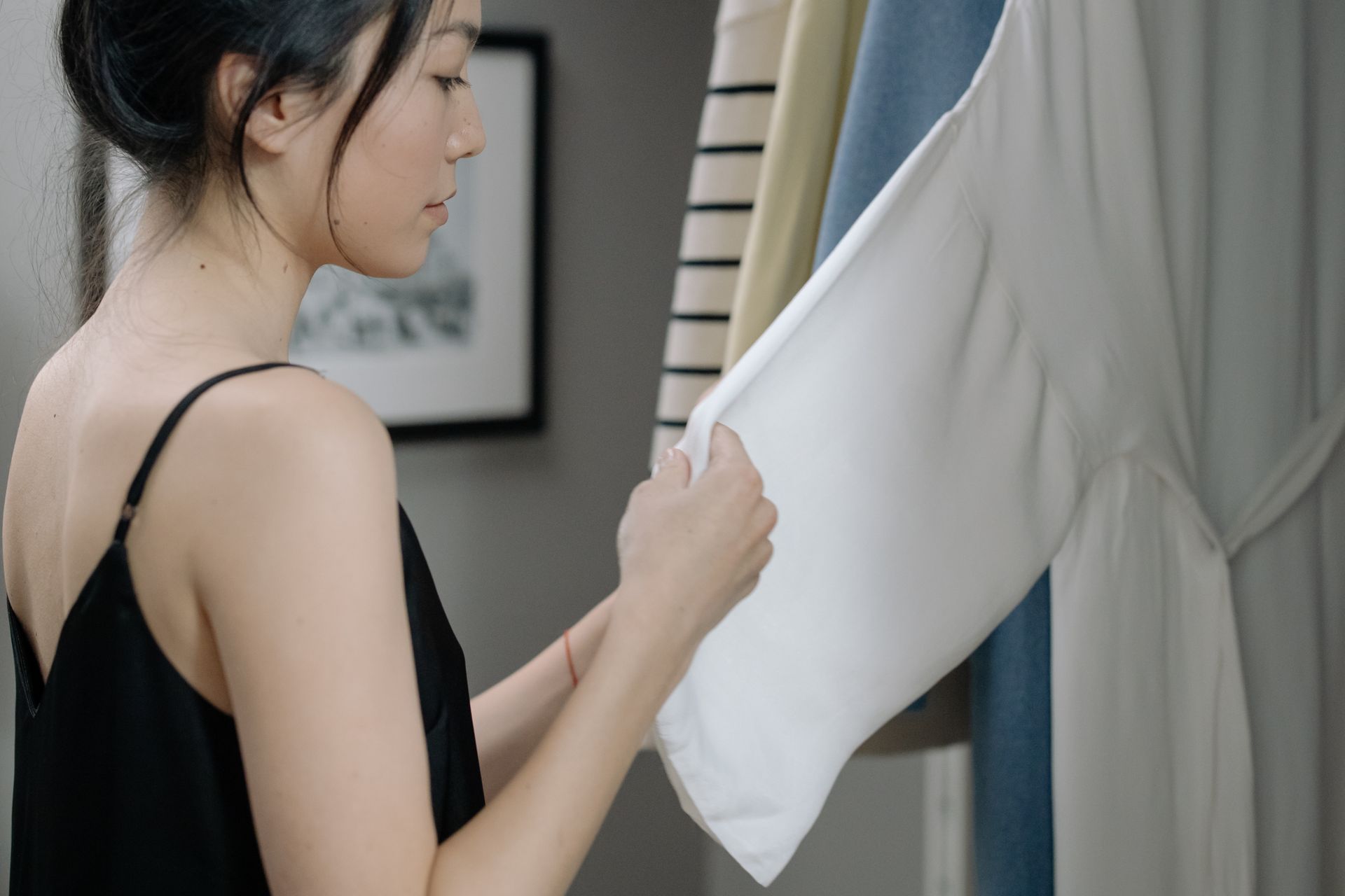 A woman in a black top selecting clothes from a cozy home closet, emphasizing style and choice.