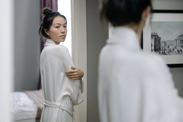 Woman In White Bathrobe Looking At The Mirror