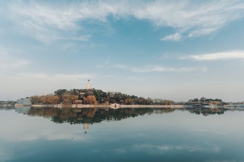 Free Scenic view of a historic tower surrounded by autumn trees, reflected in a calm lake under a clear sky. Stock Photo
