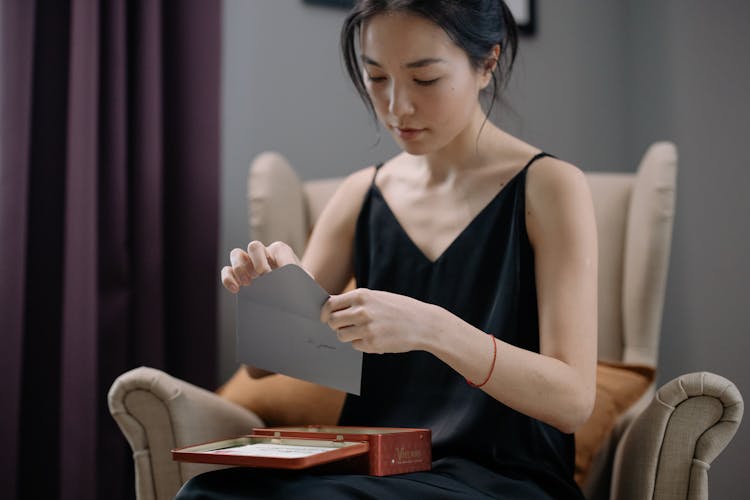 A Woman In A Black Dress Opening An Envelope