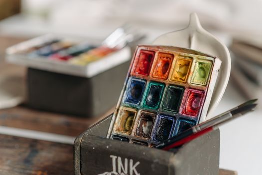 Vibrant watercolor paints and brushes in an artist's studio, ready for creativity.