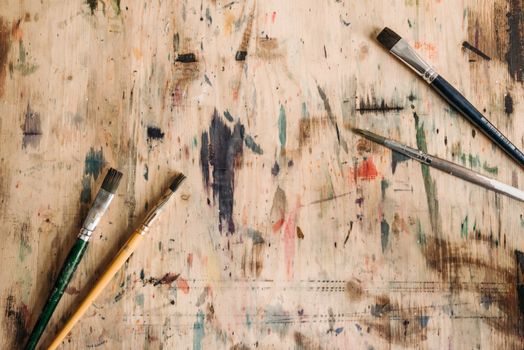 Close-up of paintbrushes with colorful paint marks on a wooden surface.