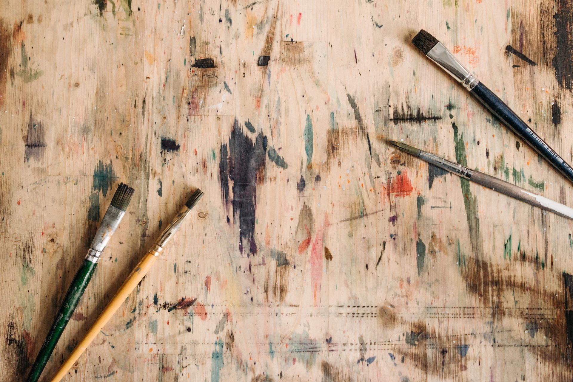 Close-up of paintbrushes with colorful paint marks on a wooden surface.