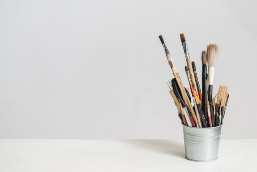 A collection of various paint brushes in a tin can against a minimalistic background.