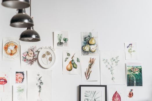 A curated collection of watercolor artworks on a white studio wall featuring fruits and plants.