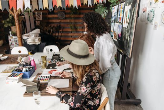 Women engaged in a creative art workshop painting with watercolors indoors.