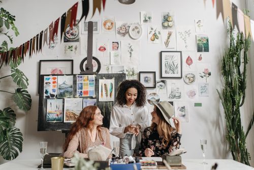 Free Three women enjoying a creative art workshop with paintings and plants around them. Stock Photo