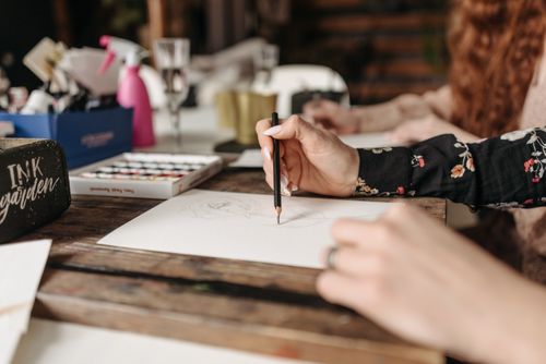 Free Close-up of a woman's hand holding a pencil, drawing on paper in an artistic setting. Stock Photo
