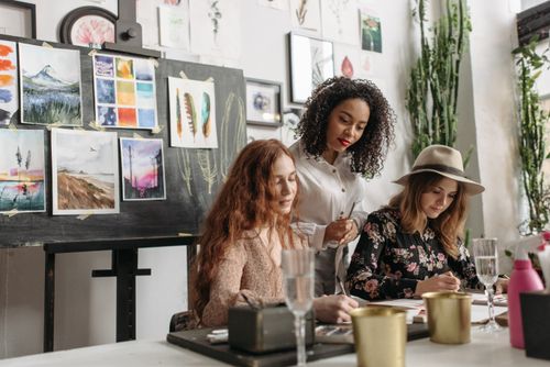 Free Three women engaged in a creative art workshop, painting in a well-lit room with artwork displays. Stock Photo