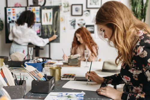 Free Focused artists engage in painting and drawing in a vibrant workshop setting, surrounded by art materials. Stock Photo