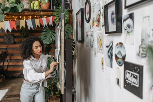 Free Woman in white shirt engaged in creative art-making on a blackboard, surrounded by artistic decor and plants. Stock Photo