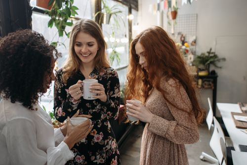 Free Three women sharing warm beverages in a cozy indoor setting with plants. Stock Photo