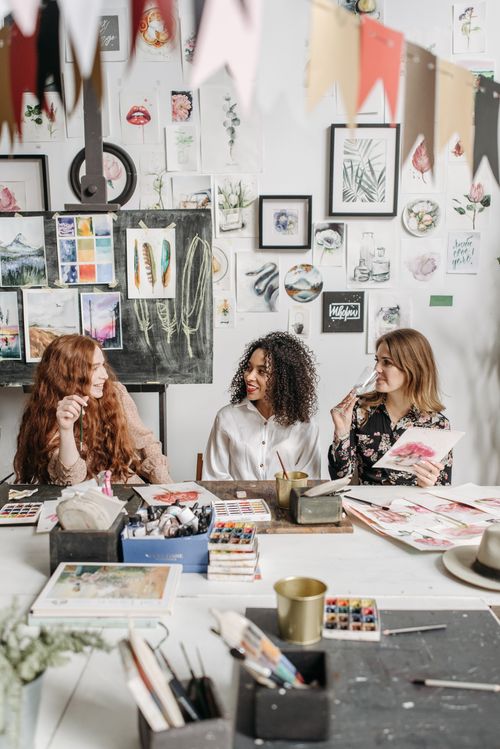 Free Three women engaged in a lively art workshop surrounded by colorful drawings and materials. Stock Photo