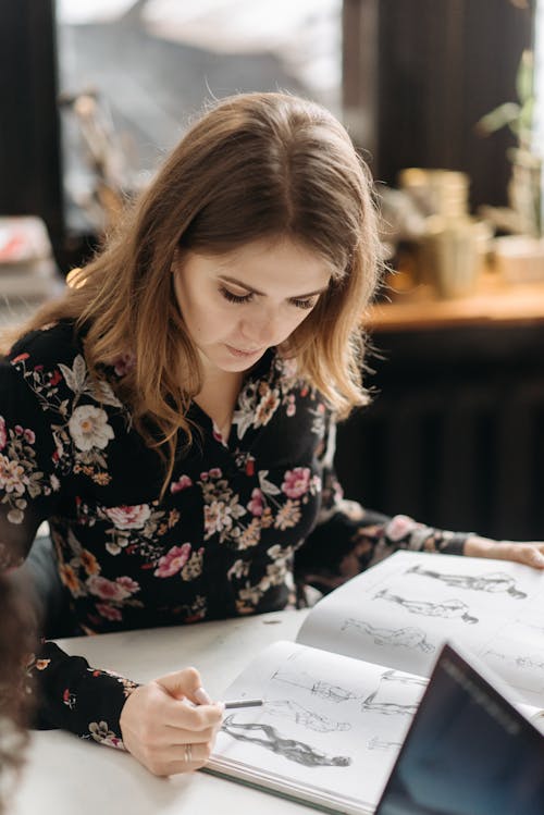 Woman in a Floral Long Sleeves Top Holding a Sketchbook