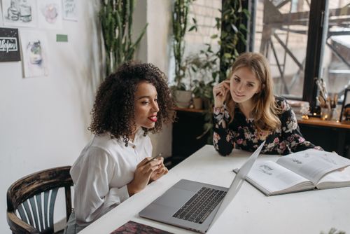 Free Two women collaborating in a modern office setting with laptop and open book. Stock Photo