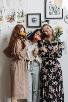Three women smiling with flowers in a cozy artistic workspace showcasing friendship and creativity.