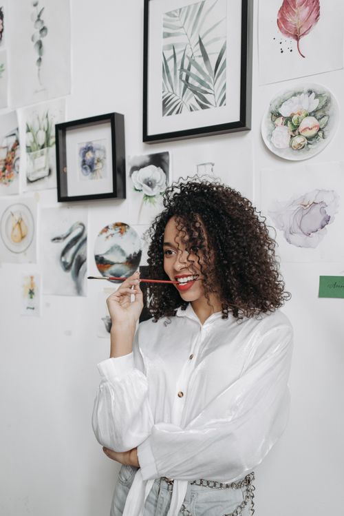 Free Cheerful woman with curly hair holding a paintbrush in a bright art studio. Stock Photo
