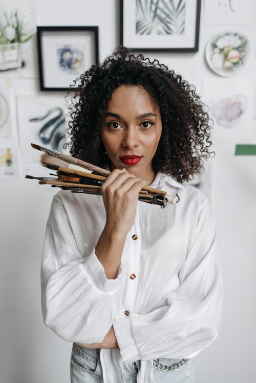 Free An African American woman holding paintbrushes in a creative studio setting. Artistic and serious. Stock Photo