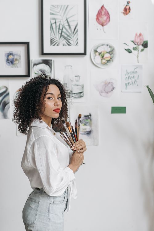 Free Elegant woman artist holding paintbrushes, surrounded by watercolor paintings indoors. Stock Photo