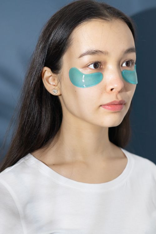 Free A woman in a white shirt wearing teal under eye patches for skincare. Stock Photo
