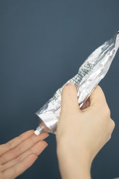 Close-up of hands applying cream from a metallic tube against a solid background.