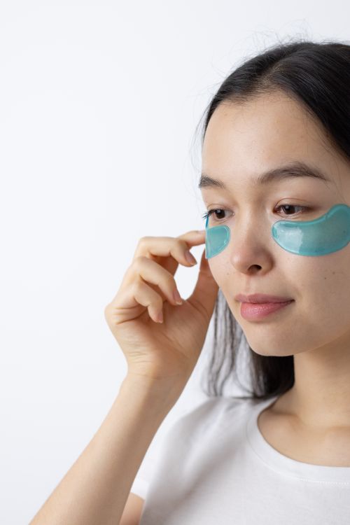 Free Portrait of a woman applying under eye patches, focusing on skincare routine. Stock Photo