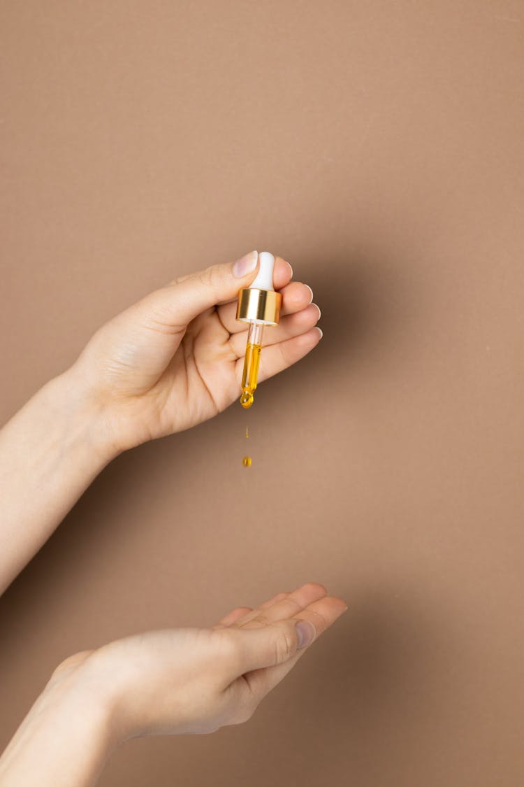 A Person Holding White And Gold Dropper