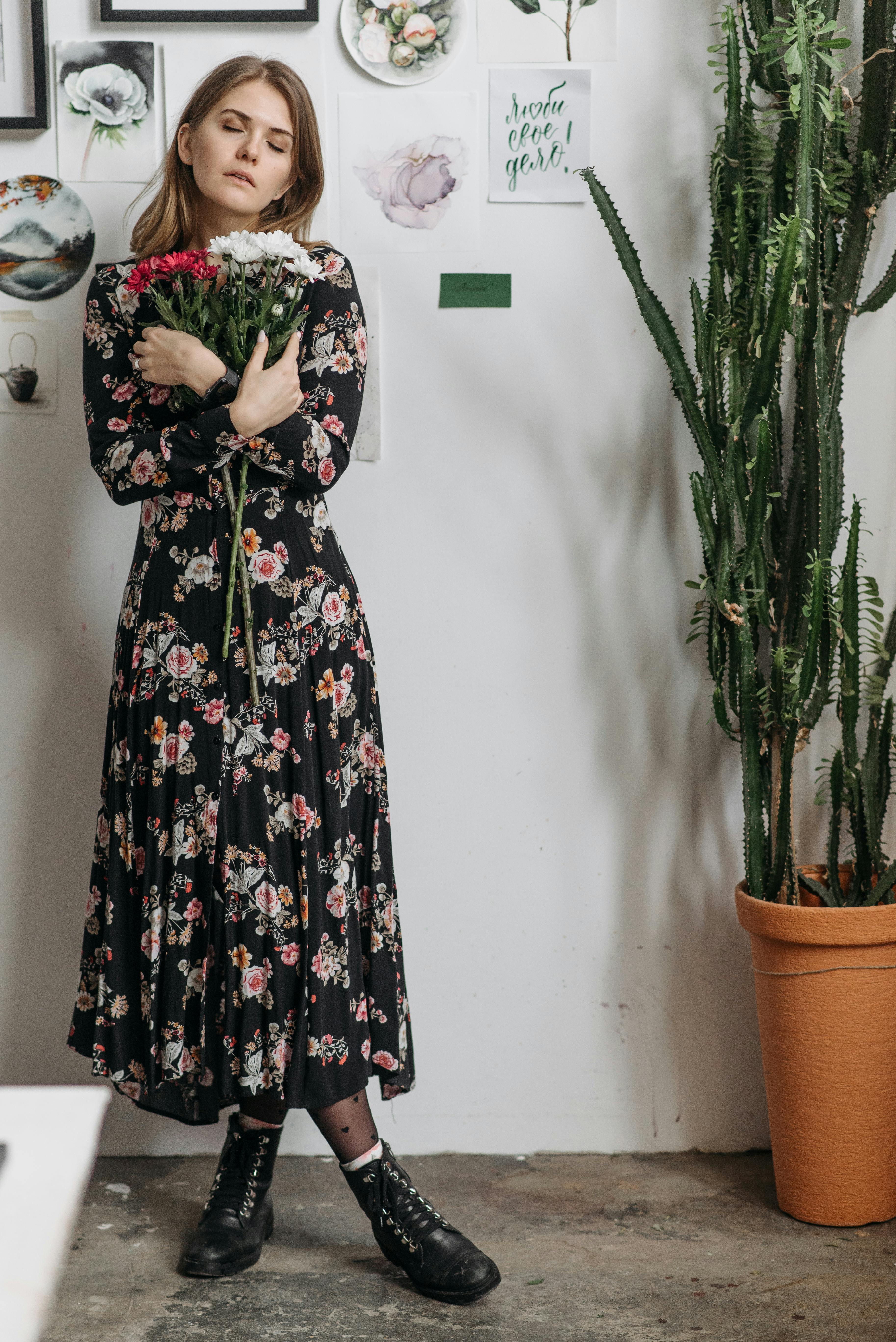woman in black floral dress standing beside cactus plant
