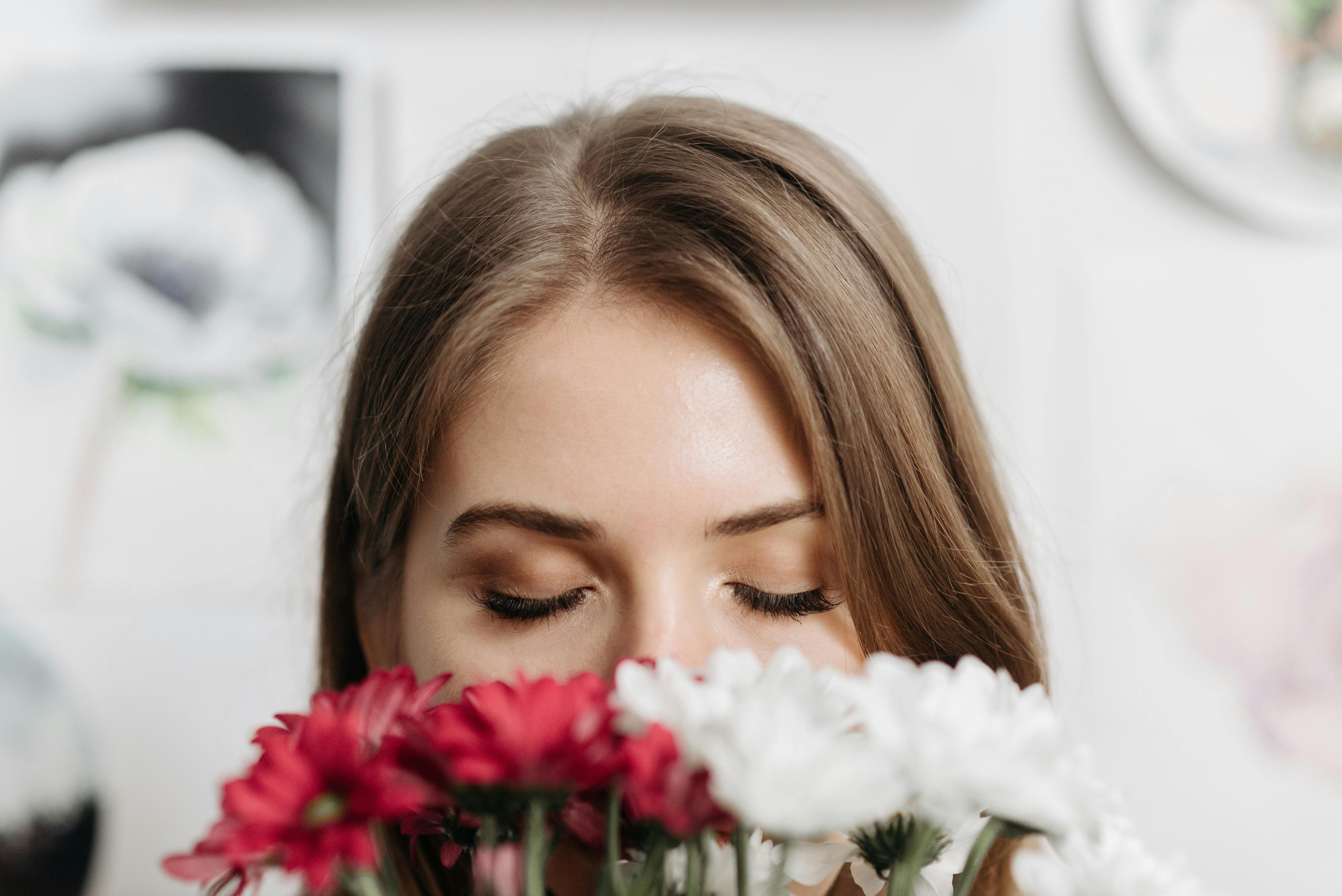 Portrait of a woman in a serene moment, eyes closed, enjoying the fragrance of vibrant flowers.