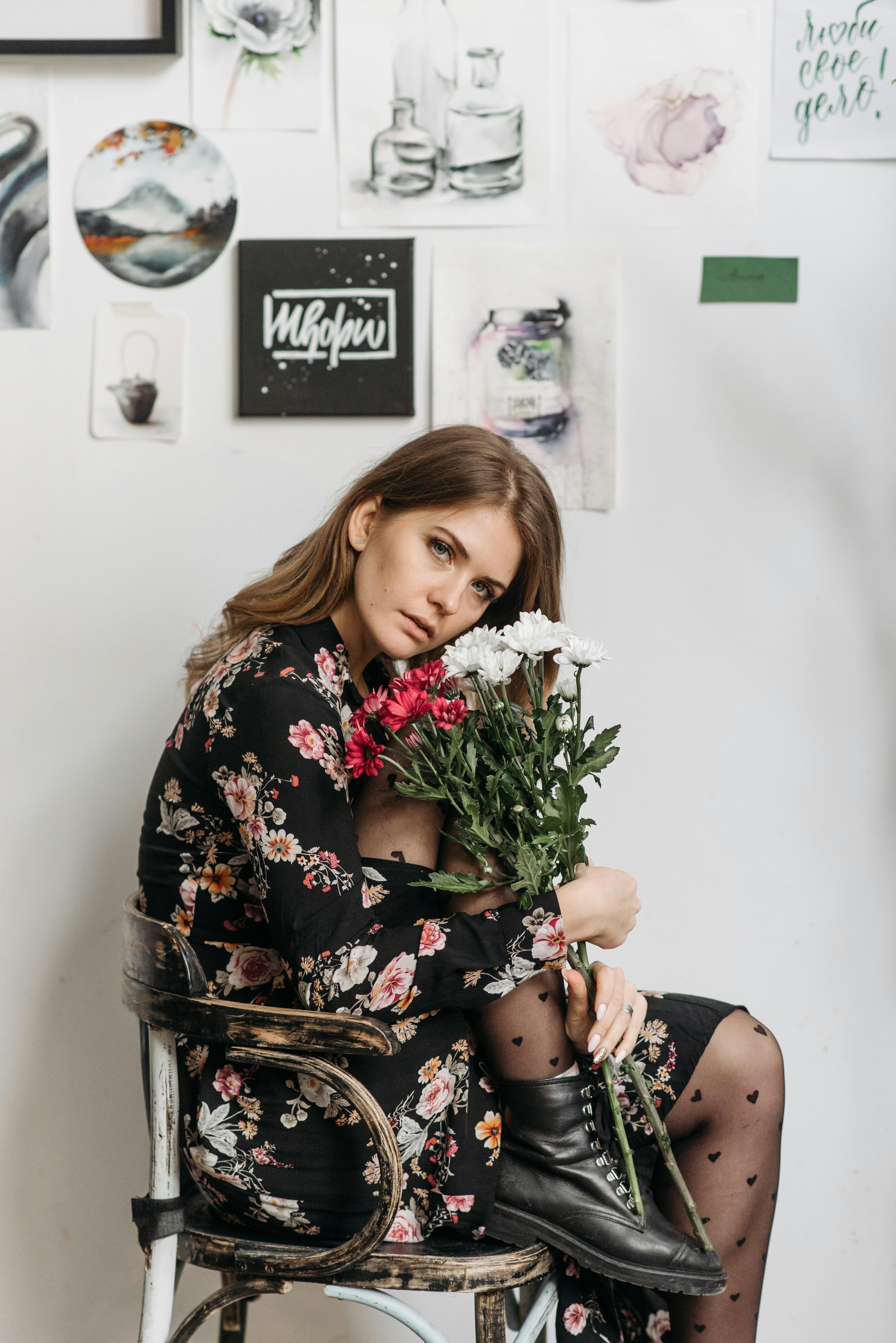 a woman in black floral dress sitting while holding flowers