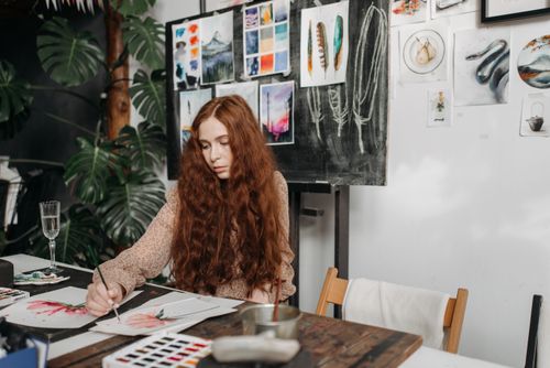 Free Young female artist painting in a vibrant studio filled with artwork. Stock Photo